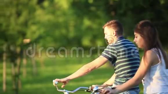 快乐的一对夫妇在公园里骑自行车夏日时光日落视频的预览图