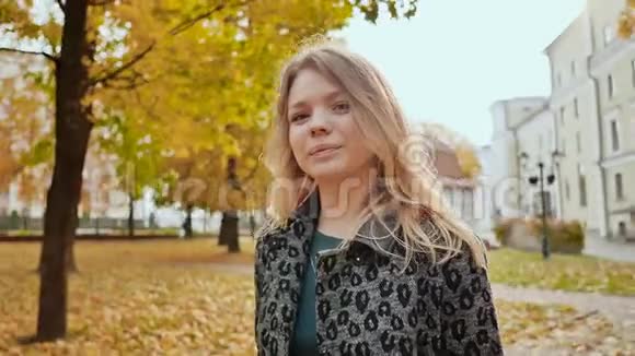 一个年轻的女孩高兴地在相机上摆着一束五颜六色的叶子秋天在城市公园散步视频的预览图