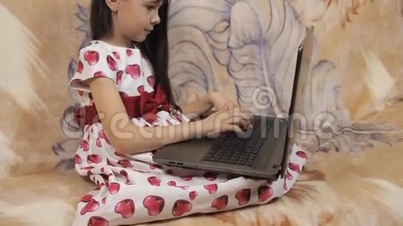 带手提电脑的孩子在沙发上穿着漂亮裙子的小女孩穿着红心衣服的女孩视频的预览图