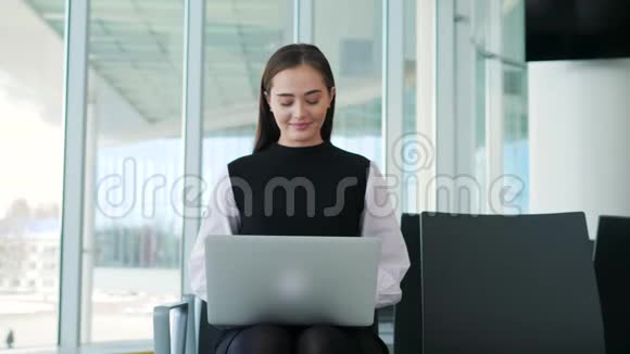机场年轻女性乘客在候机大厅坐着智能手机和笔记本电脑等待她的航班工作视频的预览图