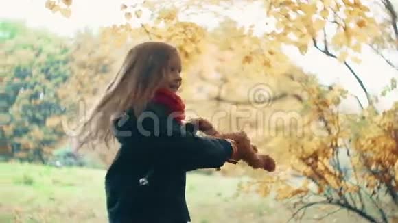 特写搞笑欢快可爱的小女孩与她的玩具旋转泰迪熊黄色在惊人的秋天公园慢动作视频的预览图
