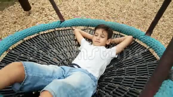 男孩在秋千上摆动吊床在城市的游乐园里4k复制空间视频的预览图