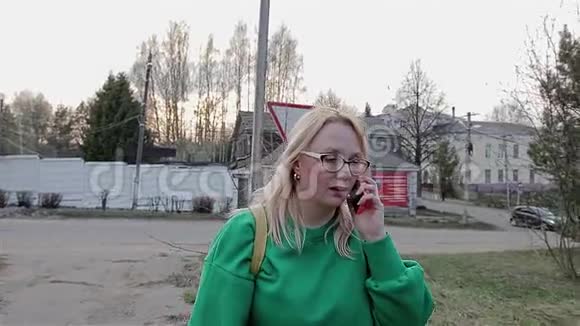 一个穿绿色毛衣的女孩在市郊用手机说话相机和她一起移动视频的预览图