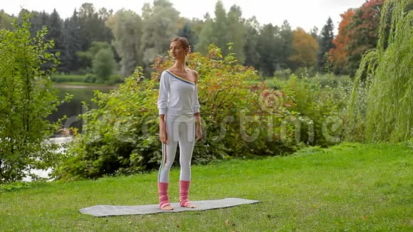 年轻女子站在河岸的防滑垫上做瑜伽运动视频的预览图