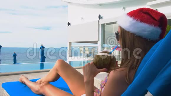 戴圣诞帽的白种人年轻女人在日光浴中喝椰子视频的预览图