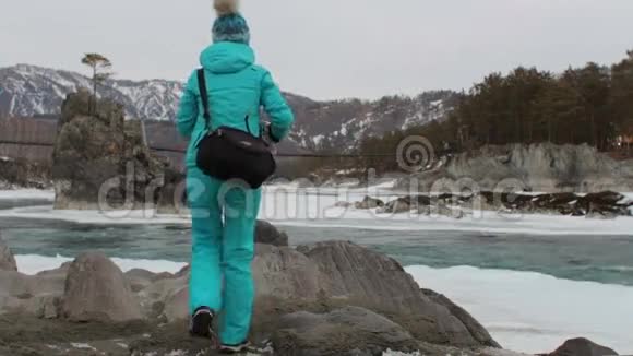 独自一个女游客在河边攀岩环顾四周冬天群山覆盖着白雪视频的预览图