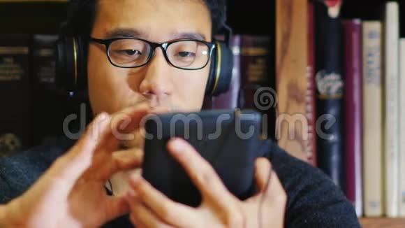戴眼镜的亚洲人的肖像它在图书馆里用平板电脑他坐在书架的背景上视频的预览图