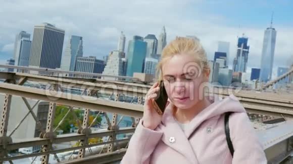 一个穿着粉红色外套的游客在打电话站在曼哈顿的布鲁克林大桥上视频的预览图