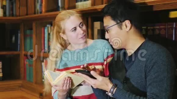韩国男人和高加索女人在图书馆看书交流使用你的平板电脑视频的预览图
