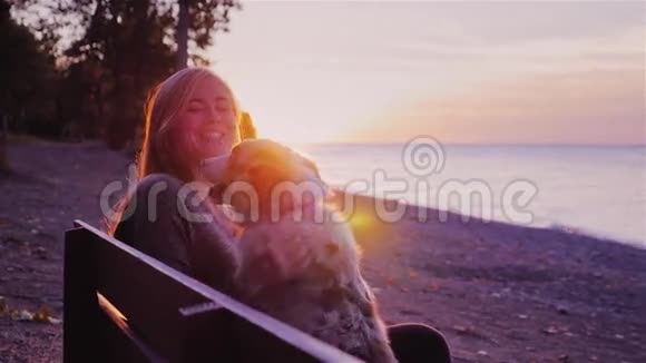 漂亮的女人和她的狗玩坐在公园的长凳上背景是美丽的日落视频的预览图