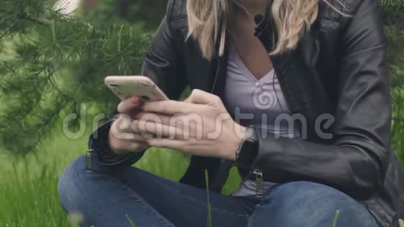 女人坐在草地上手里拿着手机和一只智能手表库存日常技术概念视频的预览图