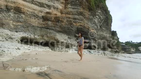 年轻的n款黑色泳衣和条纹衬衫正沿着巴厘岛海湾的沙滩漫步望着大海视频的预览图
