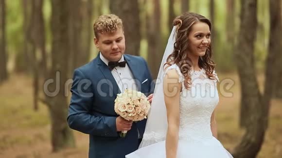 结婚在新鲜空气中的森林里快乐的一对优雅的新郎在新娘后面手中捧着一束美丽的视频的预览图
