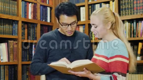 勤奋的韩国男人和高加索女人站在一起在图书馆里看书视频的预览图