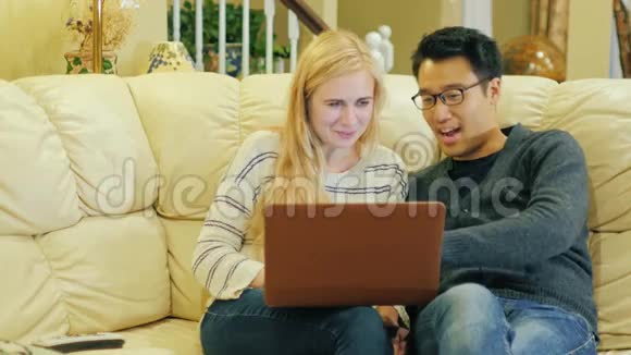朋友年轻的韩国男人和高加索女人在家休息好好享受笔记本电脑吧视频的预览图