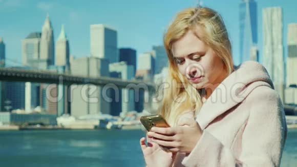 纽约在曼哈顿和布鲁克林大桥的背景下游客穿着粉红色的外套在你的智能手机上打字视频的预览图
