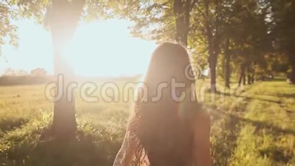 一个留着长发的漂亮女孩走在树间的绿色小径上盘旋着享受着阳光和自然视频的预览图