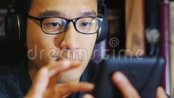 戴眼镜的韩国男人的肖像她正在使用数字平板电脑在耳机上听音乐视频的预览图