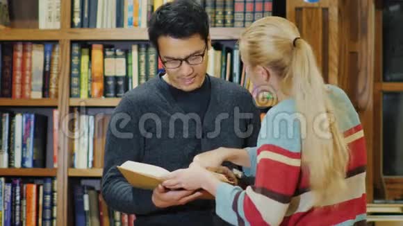 戴眼镜的亚洲男人和高加索女人站在一起在图书馆里看书视频的预览图