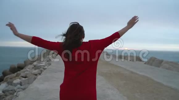 穿着红色衣服的女人跑到海边的灯塔视频的预览图