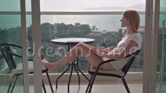 美丽迷人的女人坐在阳台的椅子上欣赏风景站起来进去视频的预览图