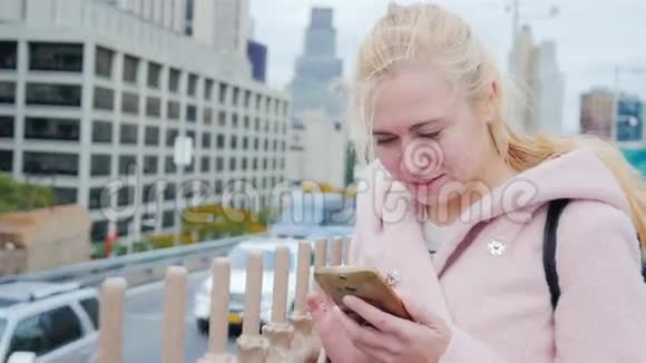 纽约一个大城市的年轻白人妇女在摩天大楼和公路的背景下用智能手机打字视频的预览图