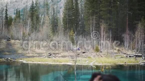 快乐的女孩旅行者坐在岩石上看着一个山坑湖穿着牛仔裤徒步旅行夹克和徒步旅行视频的预览图