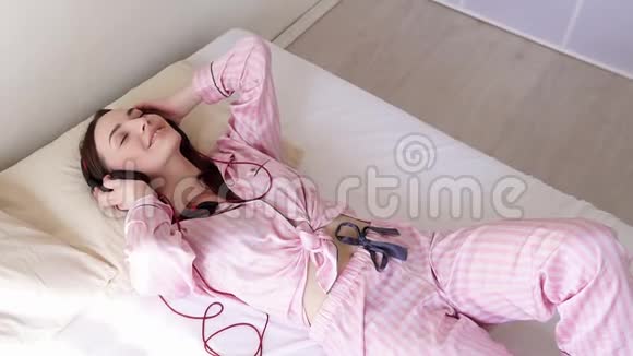 穿着睡衣的女人躺在床上用耳机随着音乐跳舞视频的预览图