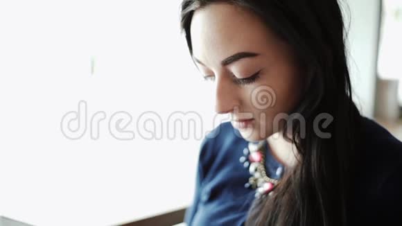 美丽的女孩黑发年轻的女人坐在一家咖啡馆在窗户旁边读一本杂志的书视频的预览图