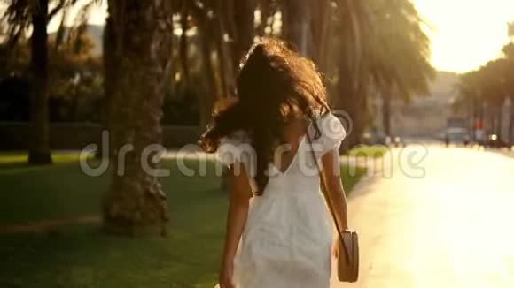 穿着白色裙子的女孩沿着棕榈树露台散步视频的预览图