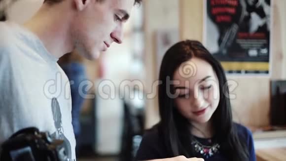 坐在咖啡馆里的漂亮年轻女子男子在靠窗的智能手机里展示了一些东西视频的预览图