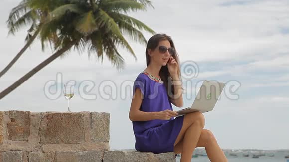 海滩上有笔记本电脑和手机的年轻女人视频的预览图