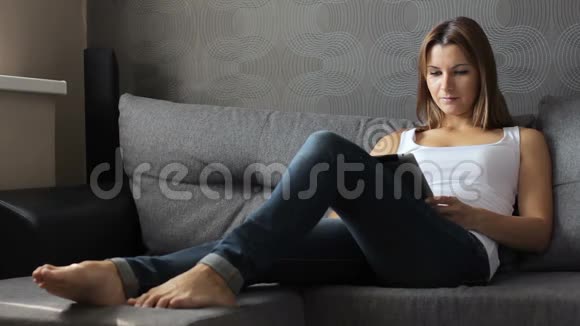 带电片的女人有平板电脑的女人坐在沙发上使用触摸屏平板电脑的女性视频的预览图