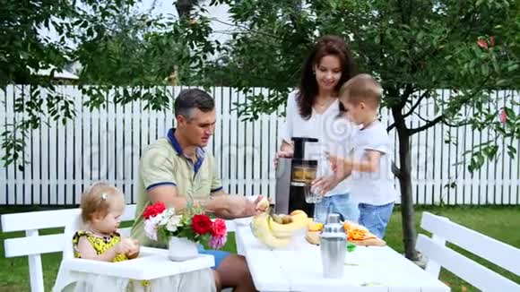 幸福美丽的家庭妈妈爸爸四岁的儿子和一岁的女儿做新鲜果汁在夏天在视频的预览图