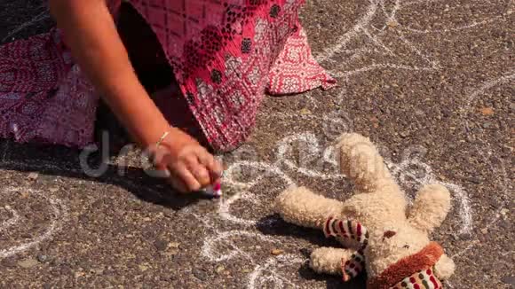 女孩用粉笔在玩具熊周围的人行道上画长画视频的预览图