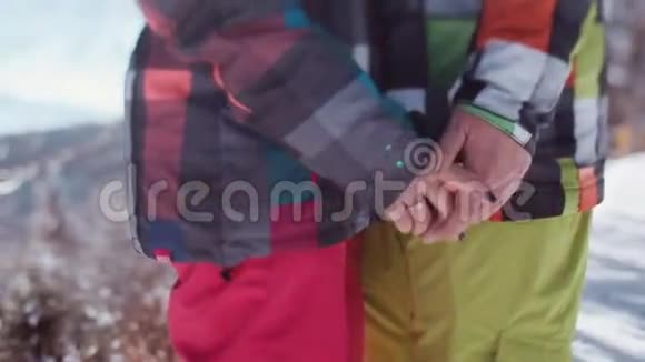 穿着粉红色滑雪服的年轻女孩和穿着绿色冬季运动服装的英俊青年别人牵着手视频的预览图