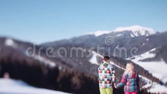 穿着粉红色滑雪服的年轻女孩和穿着绿色冬季运动服装的英俊青年可爱的一对夫妇在想视频的预览图