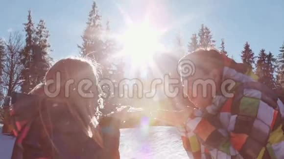 可爱的年轻夫妇穿着冬季运动服阳光明媚的冬日快乐的金发女孩和男孩互相吹雪视频的预览图