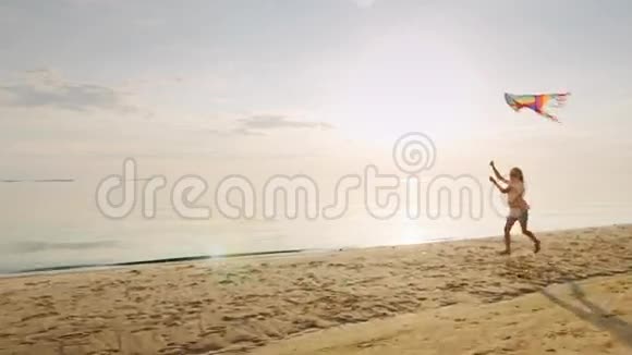 快乐的金发小女孩带着风筝跑步在日落的海边视频的预览图