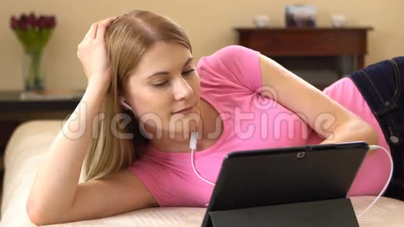 美丽迷人的年轻女子躺在沙发上在平板电脑上看电影微笑着视频的预览图