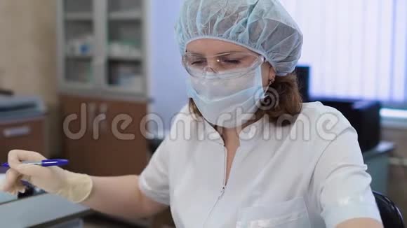 女性研究助理穿着白色实验室外套防护面罩帽子和手套坐在医学实验室工作视频的预览图