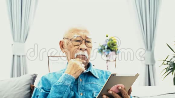 带着白胡子的亚洲老人在家里用平板电脑视频的预览图