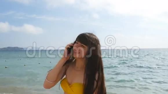 穿着泳衣的年轻迷人的女人正在海边的手机上聊天穿比基尼的快乐女孩视频的预览图