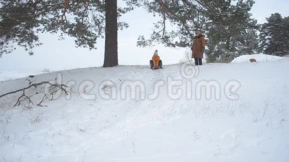 女孩笑冬天从公园的山上滚来滚去快乐的孩子在雪地里笑视频的预览图