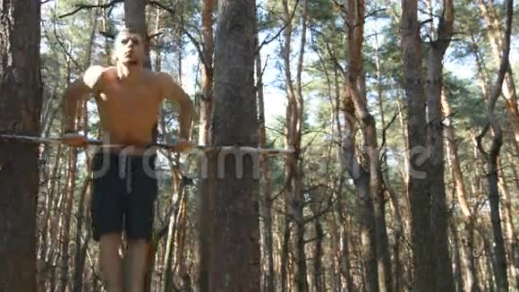 在森林里的水平杆上做俯卧撑的运动员强壮的年轻肌肉男夏季在树林里训练视频的预览图