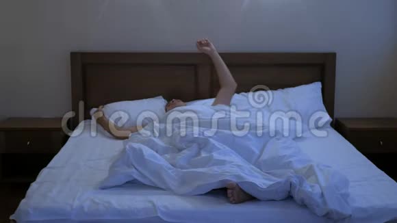 躺在床上的年轻人用枕头捂住他的头和耳朵因为他不想醒来因为他患有嘈杂的警报视频的预览图