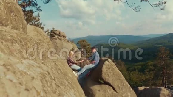 两个年轻的恋人正坐在山上的一块岩石上牵着他们的手几个进球快乐视频的预览图