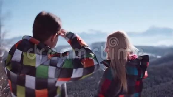 可爱的夫妇穿着五颜六色的滑雪服站在观景台上看着华丽的山脉浪漫浪漫视频的预览图