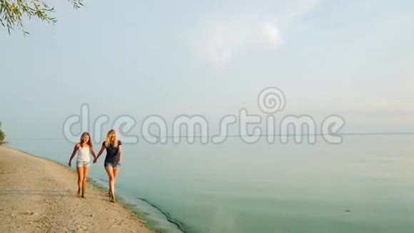 妈妈和女儿沿着风景如画的海滩散步那里的蓝天和水混合在一起视频的预览图