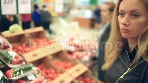 一个女人在蔬菜货架上的超市里买蔬菜和水果男人选择番茄视频的预览图